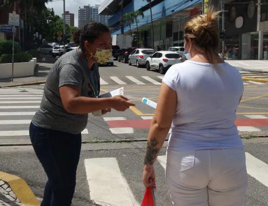 mulher de máscara entrega panfleto para outra mulher